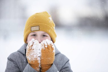Kışın çocuk. Sıcak şapkalı ve eldivenli küçük bir çocuk kameraya bakar ve gülümser..