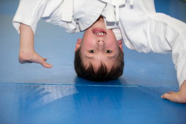 Baş aşağı duran kimano giymiş küçük bir çocuk. Çocuk judo ya da karate yapıyor. Dövüş sporları öğrencileri için bölüm.