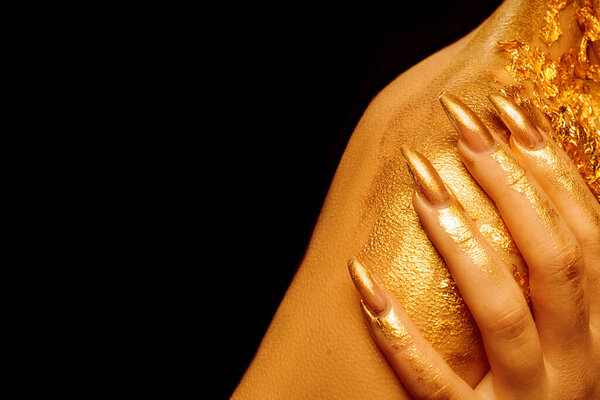 On the shoulder, fingers with golden manicure on a black background.