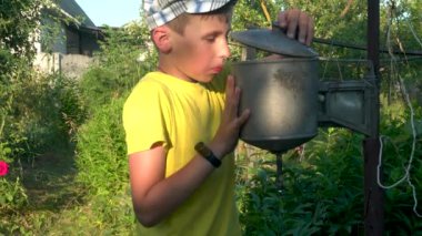 A boy in a yellow T-shirt washes his hands under the washbasin on the street in the countryside