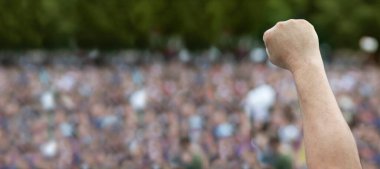 A hand in a fist in protest against a blurred crowd of people.