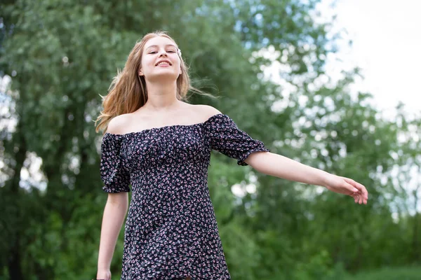 Happy young girl in a romantic dress on a green summer meadow. Beautiful teen girl smiles and looks into the camera.