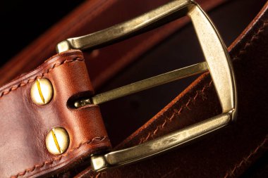 Part of a leather brown belt with a metal buckle on a black background.