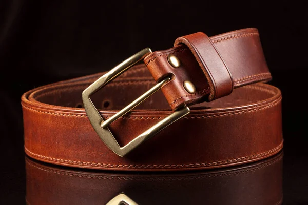 Part of a leather brown belt with a metal buckle on a black background.