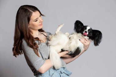 Cute young woman holding her papillon puppy. Love between owner and dog. The girl is playing with the dog.