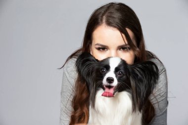 A cute young woman is hugging her papillon puppy. The eyes of a beautiful girl and the eyes of a funny dog with big ears.