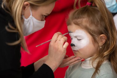 A make-up artist draws face painting on the face of a little girl.