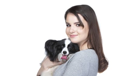 A lovely young woman is hugging her papillon puppy and looking into the cummera. Love between owner and dog. Isolated on white background.