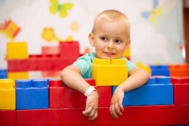 A little boy plays with a lot of colorful plastic construction blocks and builds indoors.