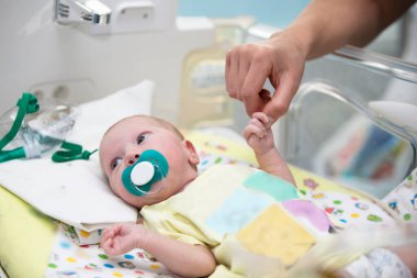 The doctor's hand holds the hand of a newborn baby in a medical box.