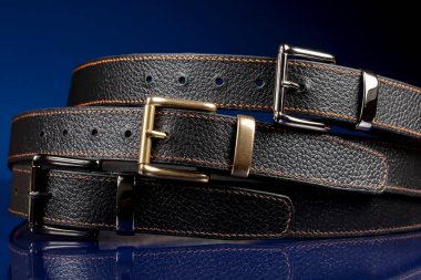 Group of black leather belts on a blue background.