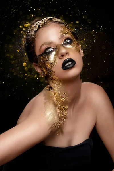 Beautiful girl with golden make-up on the background of flying golden sparkles.