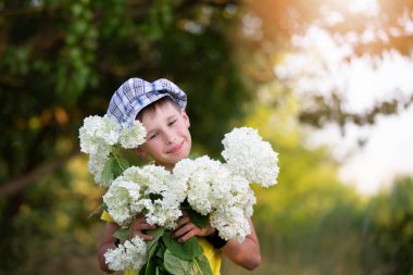 Cheerful happy village child with a bouquet of flowers. Smiling little boy with hydrangea in the garden. Mother's day, March 8, International Women's Day concept.