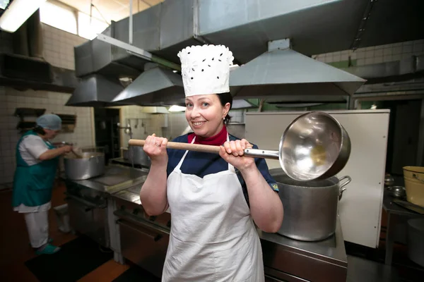 Happy industrial kitchen chef posing with big ladle. Public dining room.