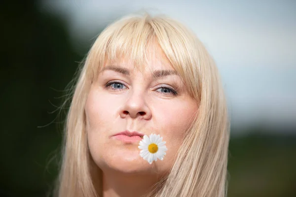 白髪の中年女性は彼女の口の中にカモミールの花を保持しています — ストック写真