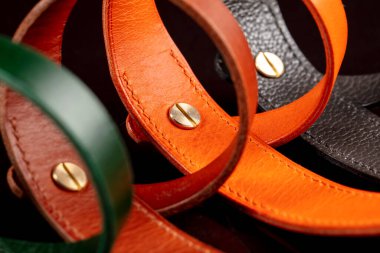 A group of multi-colored leather belts on a black background.