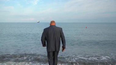 A businessman enters the sea, undressing on the go.