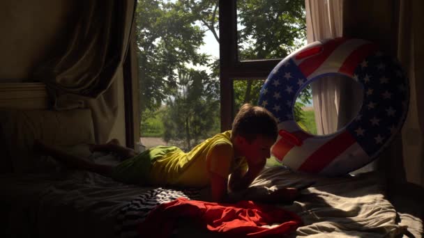 这个男孩度假时在床上玩智能手机 — 图库视频影像