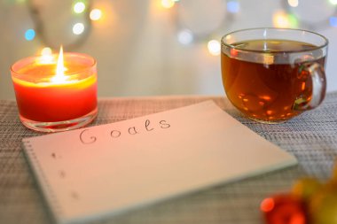 Gelecek yıl için bir Noel arkaplanı, yanan bir mum, bir fincan çay ve ışıltılı bir çelenkle planlama hedefleri. Sığ alan derinliği.