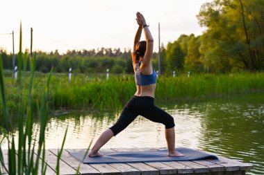 Bir kadın, doğada gölde fizyoterapi egzersizleri yapmakla meşgul. Hastalıkları egzersizle tedavi etme kavramı.
