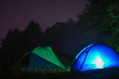 Vahşi doğadaki şehirlerden uzakta, parlak gece yıldızları arasında kamp çadırları. Macera dolu bir hayat tarzı. Seyahat tutkusu kavramı. Aktif hafta sonu tatili vahşi doğa. Yaz tatili.
