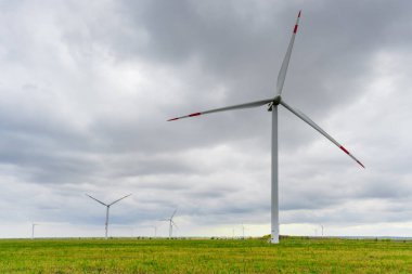 Rüzgâr parkında pervaneli büyük rüzgar türbinleri. Arka planda bulutlu gökyüzü..