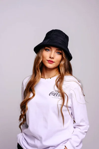 黒の帽子の美しい若い女の子は真剣に探しています 長い髪と青い目をしたモデルコピースペースとグレーの背景にミディアムアップ — ストック写真