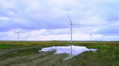 Rüzgâr parkında, arka planda bulutlu gökyüzünde büyük rüzgar türbinleri. Köy yolu. Tarladaki siluetler yel değirmenleri. Alternatif enerji.
