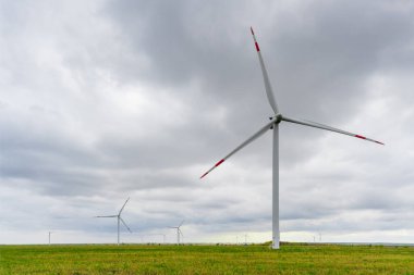 Rüzgâr parkında, arka planda bulutlu gökyüzünde büyük rüzgar türbinleri. Tarladaki siluetler yel değirmenleri. Alternatif enerji