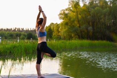 Bir kadın doğada göl üzerinde egzersiz yapıyor. Formda kalma kavramı.