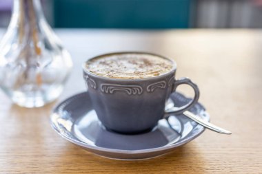 Sabah kahvesi arka planda, güneş ışığının altında, pencerenin arkasında. Güzel bir fincanda kapuçino kahvesi..