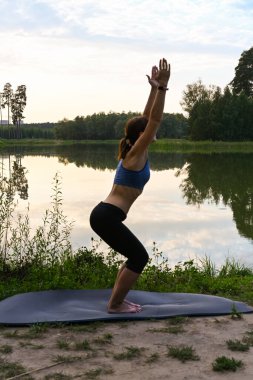 Bir kadın doğada göl üzerinde egzersiz yapıyor. Formda kalma kavramı.