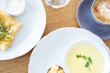 Sabah kahvaltısı peynir çorbası, kahve, kızarmış ekmek, krep ve yeşillikler ile pencerenin arka planında.