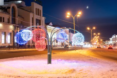 Ulyanovsk, Rusya - 14 Şubat 2022: Akşamları topları olan bir ağacın Noel figürü. Noel süslemeleri içinde karla kaplı cadde.