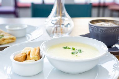 Sabah kahvaltısı peynir çorbası, kahve, kızarmış ekmek, krep ve yeşillikler ile pencerenin arka planında.