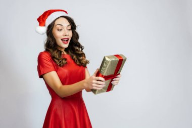 Kadın aldığı hediyeyle mutlu. Beyaz bir arka planı olan Noel şapkalı güzel bir esmer..