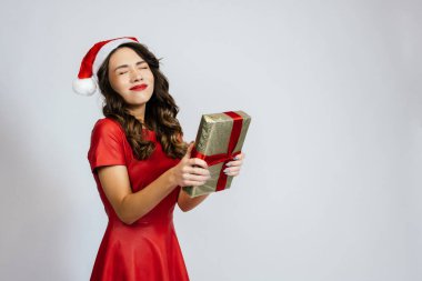 Kadın bir hediye aldığı için sevinçle gözlerini kapattı. Beyaz bir arka planı olan Noel şapkalı güzel bir esmer..