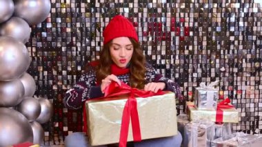 Kırmızı şapkalı güzel bir kadın, büyük bir hediyeyle eşarp yere oturur, hediyeyi büyük taşaklı parlak bir arka planda faiziyle açar..