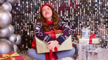Kırmızı şapkalı güzel bir kadın, büyük bir hediyeyle eşarp yerde oturur ve büyük balonlarla ışıl ışıl bir arka planda sevinir..