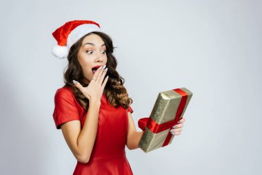 Kadın hediyeye o kadar şaşırdı ki ağzını açtı. Beyaz bir arka planı olan Noel şapkalı güzel bir esmer..