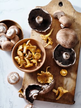 Top view various mushrooms on a wooden cutting board: portobello, champignons, chanterelles