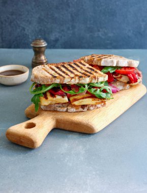 Sandwich with sourdough bread and grilled halloumi cheese on wooden cutting board