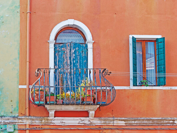 Two windows in an orange wall in Burano, Italy