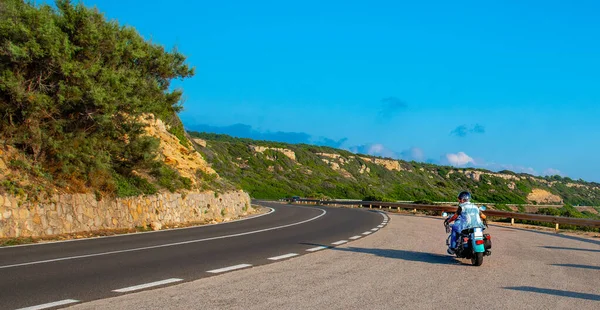 Klasik bir motosikletle gün batımında dolambaçlı bir yolda birleşen bir motorsikletli.