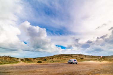 İtalya 'da Sardinya' da bulutlu bir gökyüzünün altında park etmiş gri bir SUV.