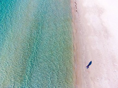 Turkuaz bir denizin kenarında duran adam yukarıdan görüldü.
