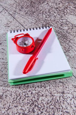 Gri arkaplanda kırmızı kalem ve alarm saati olan bir not defteri aç