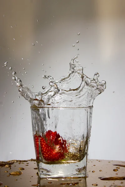 Morango cai com um respingo em um copo com água — Fotografia de Stock