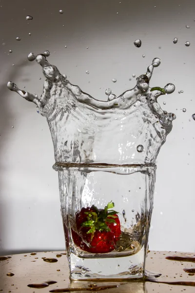 Erdbeere fällt mit einem Spritzer in ein Glas mit Wasser — Stockfoto