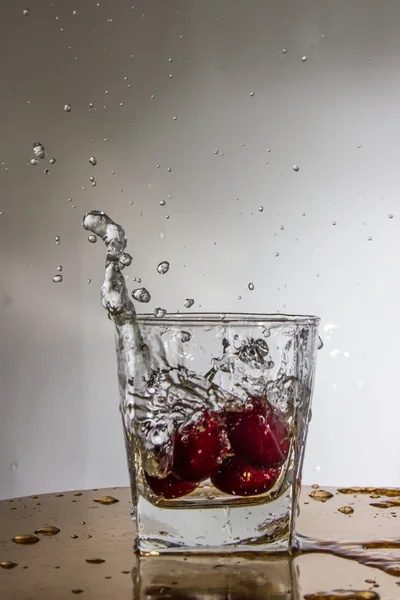 Cherry falls with a splash in a glass with water. — Stock Photo, Image